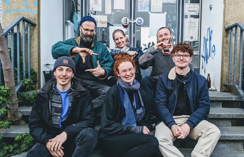 Ein Team-Foto. Zu sehen sind 6 Menschen, die auf der Treppe vor der B-Side sitzen.