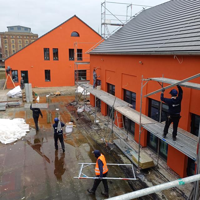 Ein Foto der Dachterasse. Es laufen Bauarbeiter*innen durch die Gegend. Die innenliegenden Wände sind jetzt orange/rot gestrichten.